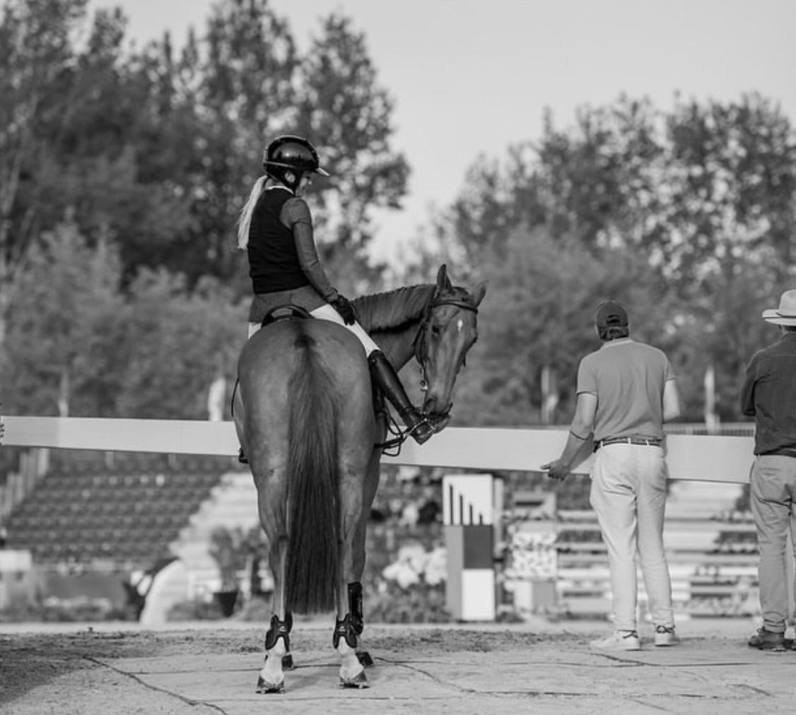 Black and white photograph of Ashlee and her horse beside the arena